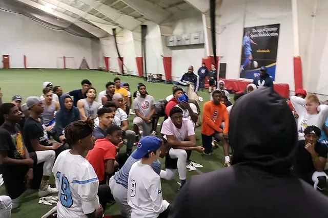 High school athletes huddled around a coach at an indoor camp