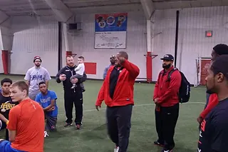 Coaches giving instruction to a seated group of athletes at an indoor camp