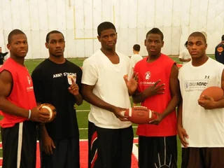 Five high school athletes at an indoor combine holding footballs
