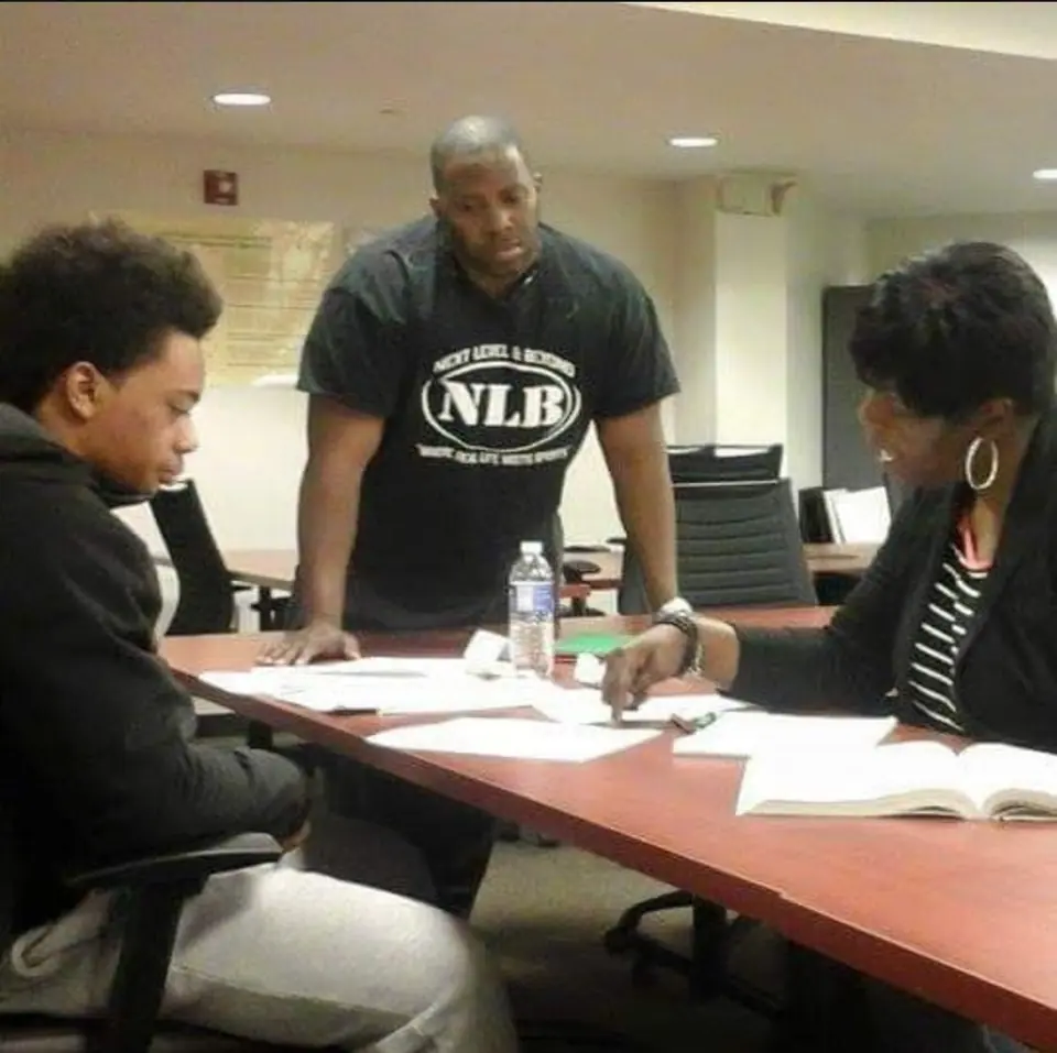 A mentor and a counselor work through paperwork with a student at a conference table