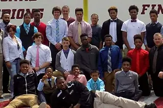 Program members in dress clothes in front of a national champions wall