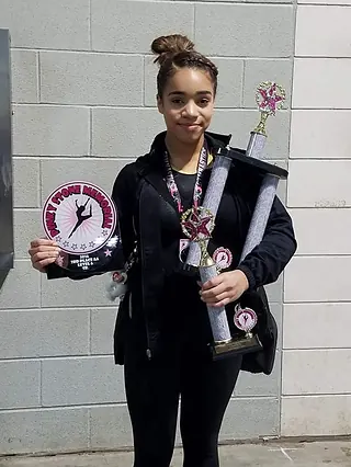 A Next Level and Beyond student athlete holding her gymnastics trophies and award banner