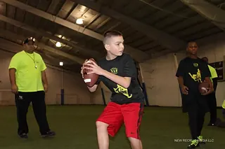 A young quarterback running a drill in a Next Level and Beyond shirt at an indoor facility