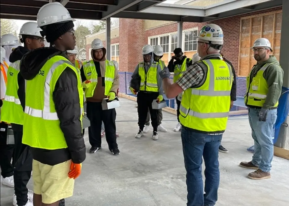 Students in hard hats and safety vests touring a construction site